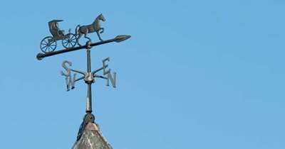 A weathervane with a horse and buggy on it against a clear blue sky