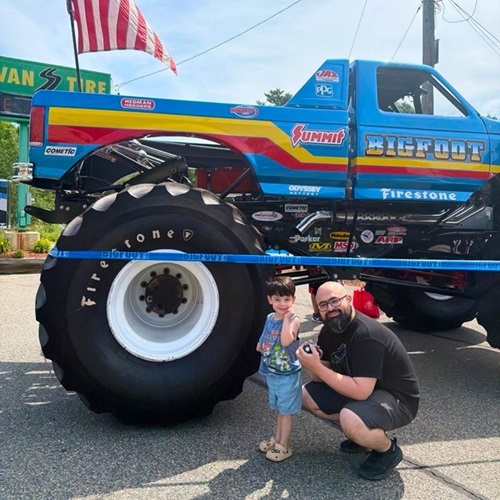 A father and son posing for a photo with the Bigfoot truck's side profile behind them