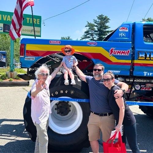 Paul Sullivan posing with a family in front of the truck, the child is sitting on the truck's large tire.