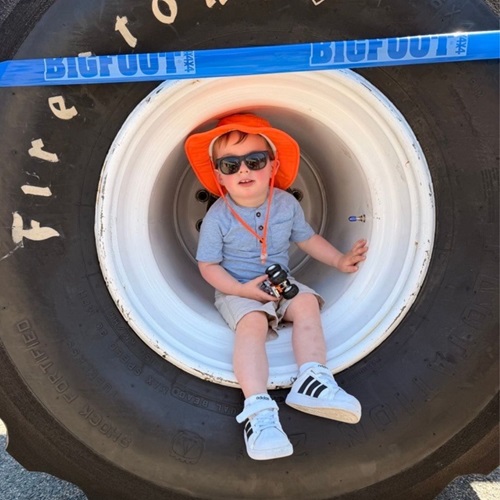 A child in an orange sunhat and sunglasses sitting inside one of Bigfoot's large tires