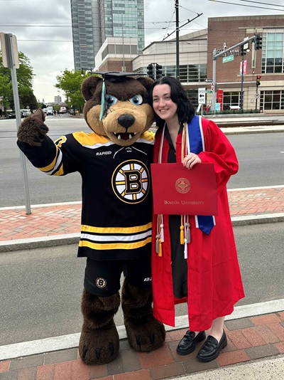 Blades the mascot posing with a BU Graduate in their robe. Blades is wearing their graduation cap.