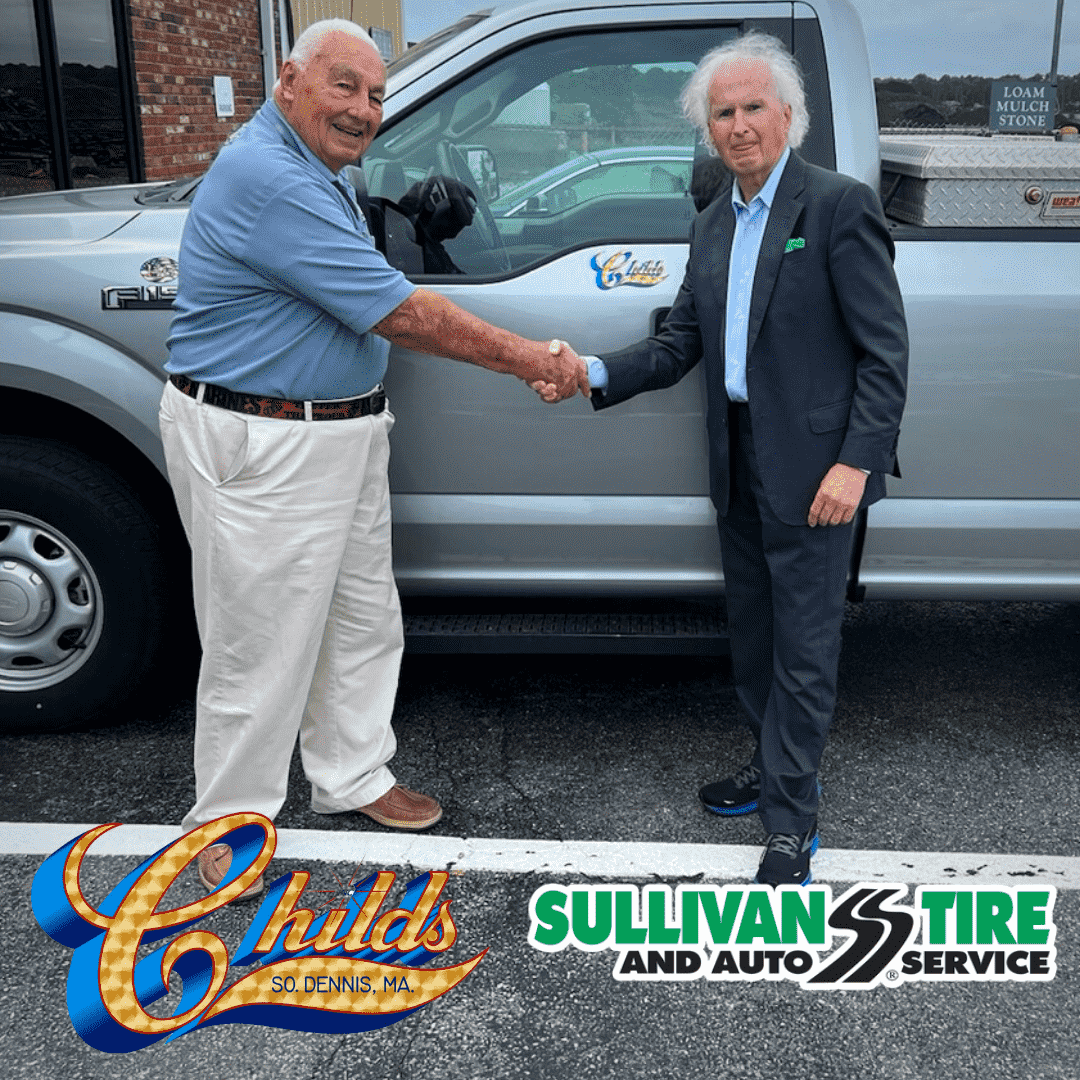 Photo of Robert Childs and Paul Sullivan shaking hands in front of a silver truck with the Childs logo on it. Beneath them is the Sullivan Tire and Childs logos.
