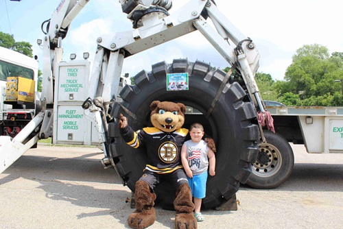 Blades the Bruins mascot posing with a child in front of a giant tire and Sullivan Tire's Commercial Boom Truck