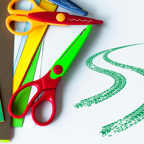 Scissors and paper against a white background. The right side of the image has green tire marks